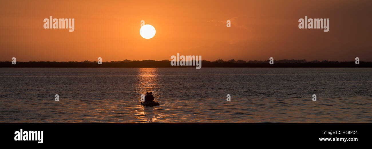 a small raft with two men in silhouette on the reflecting rays of sunrise. Stock Photo