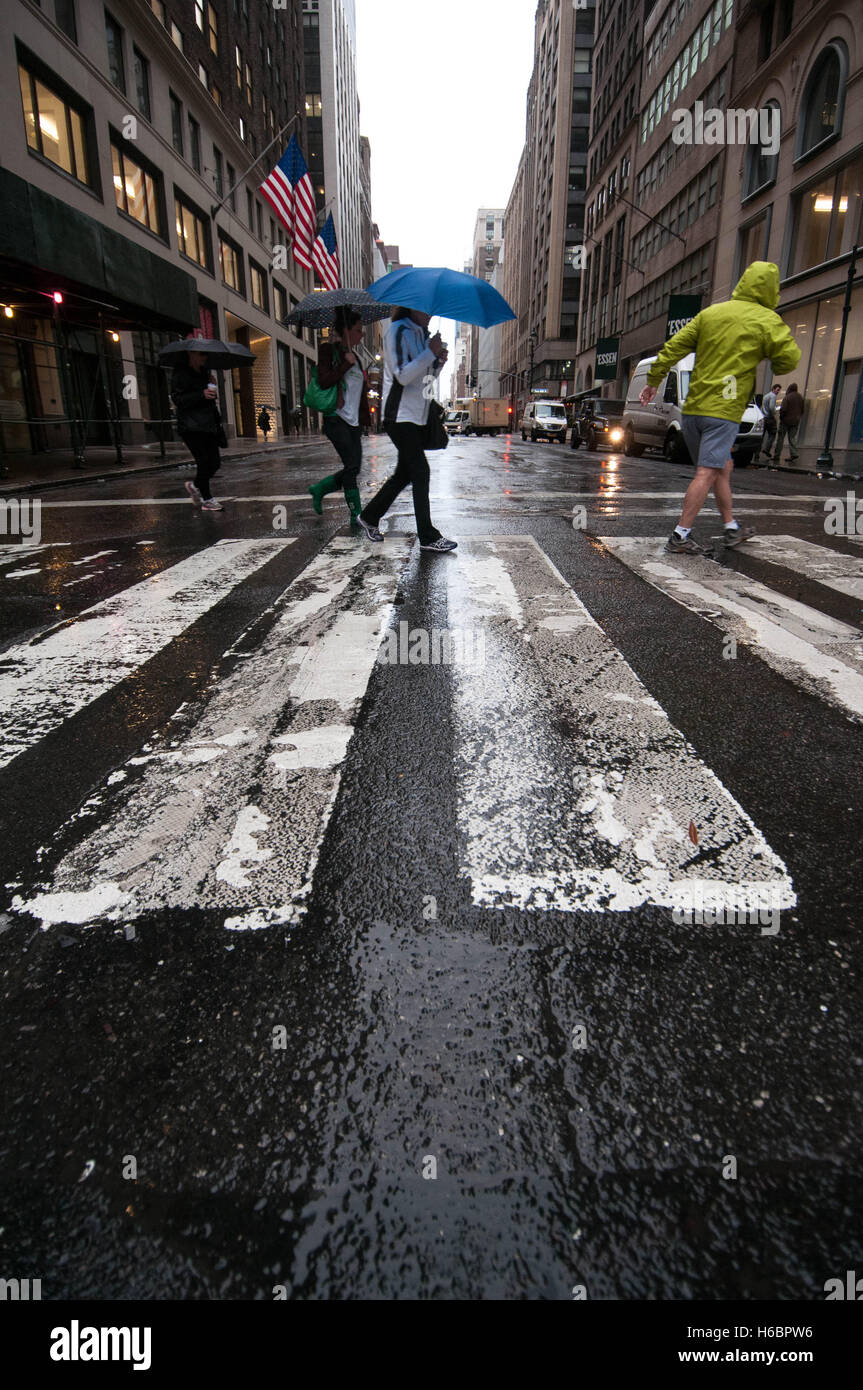 Pedestrians with umbrellas and rain jackets cross a New York City street in the rain. Stock Photo