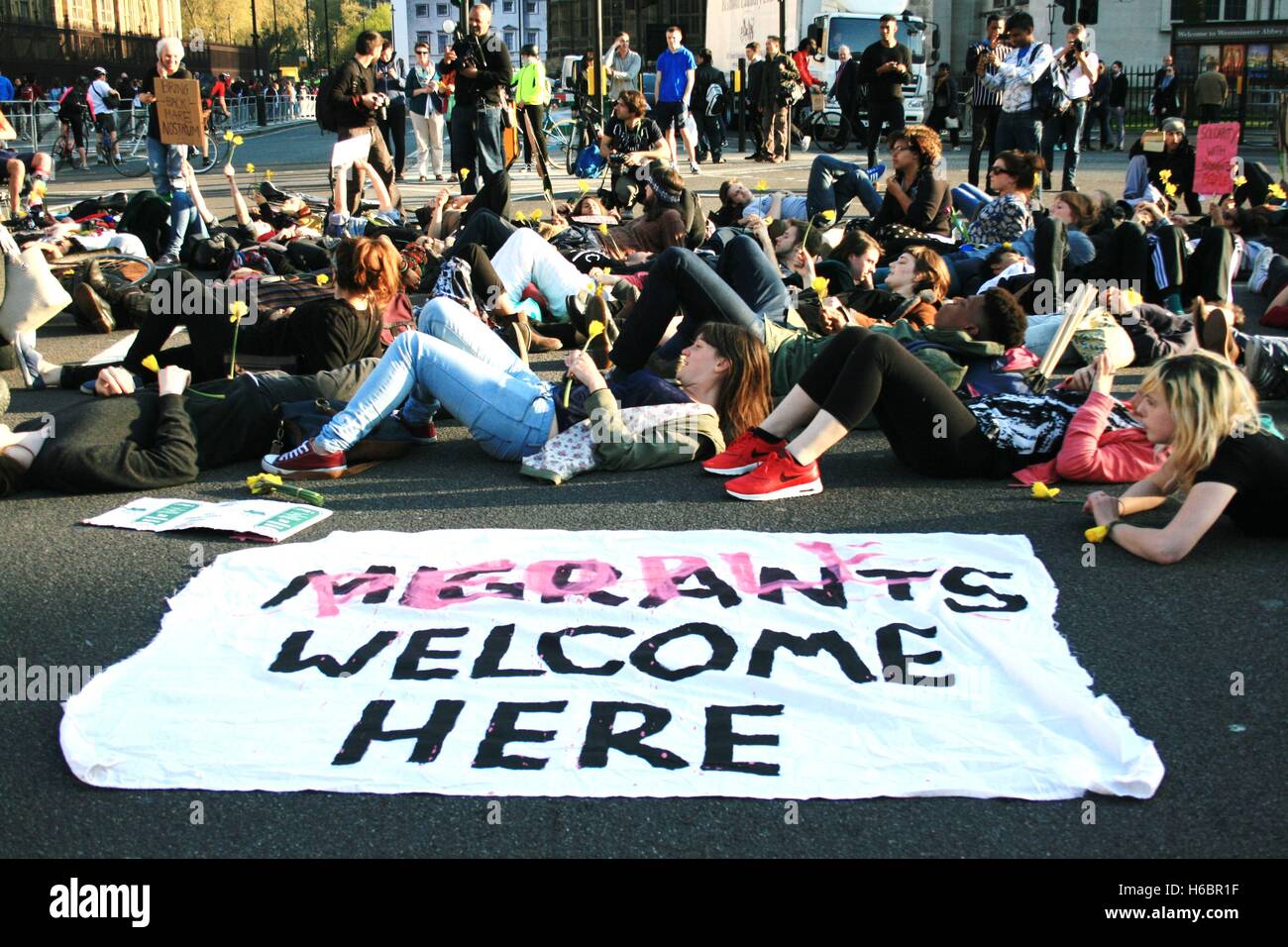 Solidarity campaigners for those who have lost their lives crossing the Mediterranean to seek a better life and refuge in Europe, stage a 'Die In' on Parliament Square, by lying on the ground to block traffic and symbolising the dead. The word 'migrant' is crossed out with the word people to highlight the language surrounding the movement of people. Stock Photo