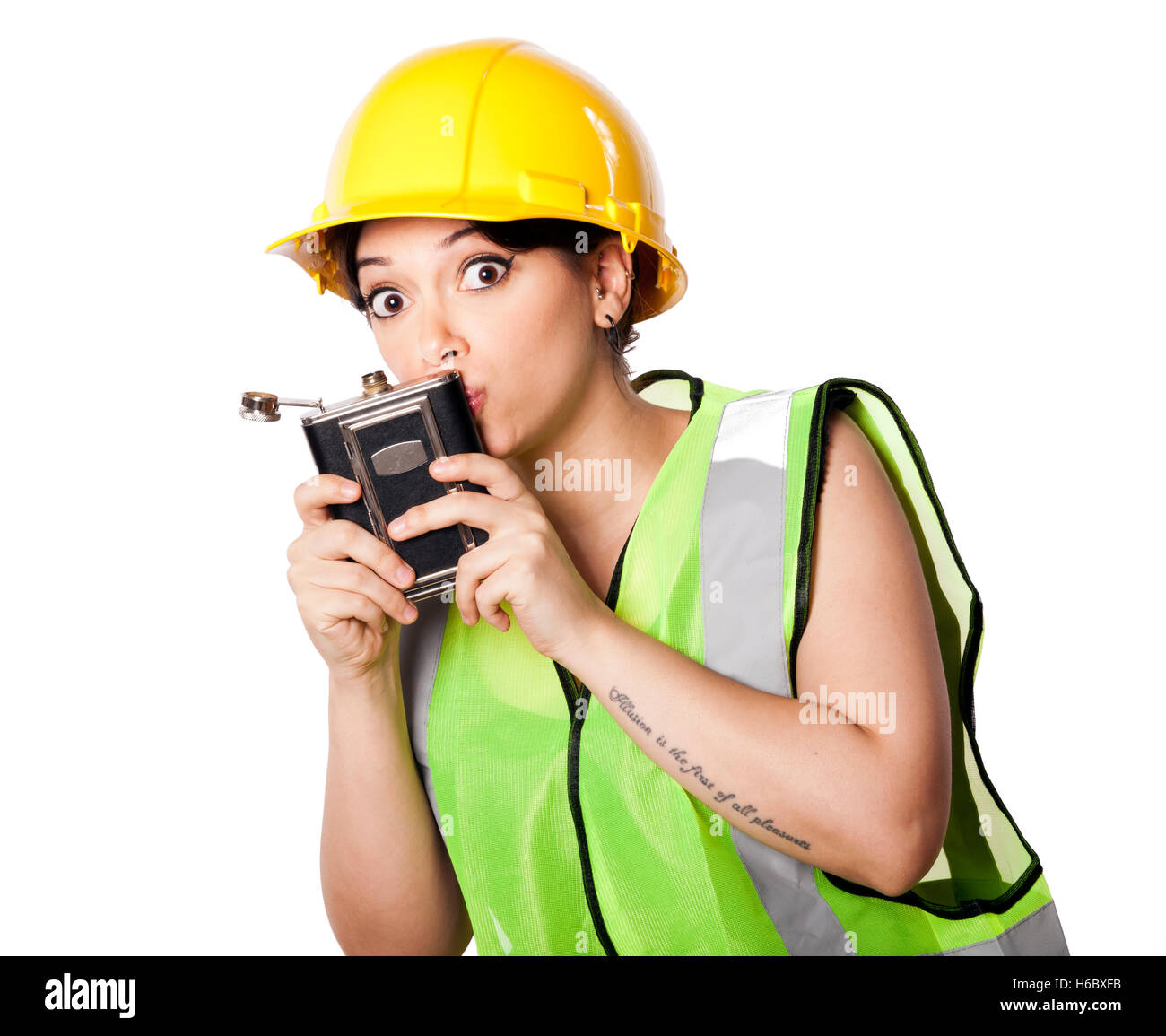 Caucasian young adult woman in her mid 20s wearing reflective yellow safety helmet and safety vest, kissing a hip flask. Isolate Stock Photo