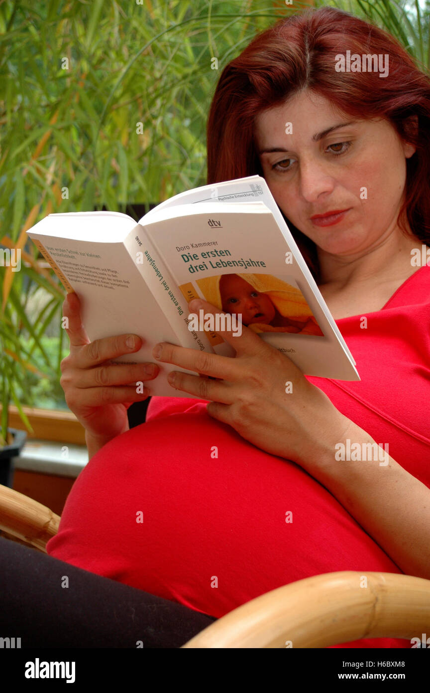 Pregnant woman reads book about babies Stock Photo