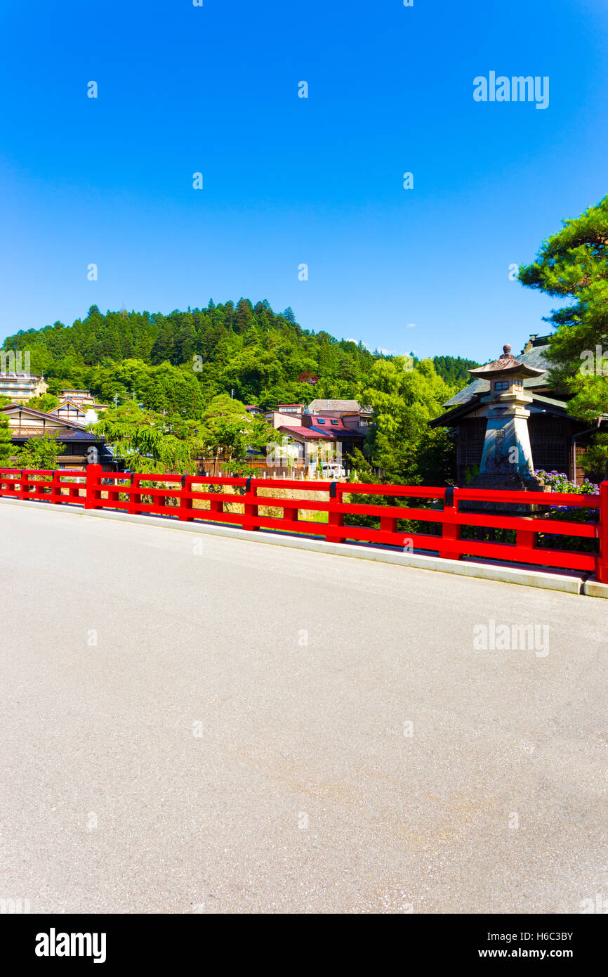 A forest mountain and blue sky behind the red Naka Bashi bridge at the entrance to historic old town in alipine city of Takayama Stock Photo