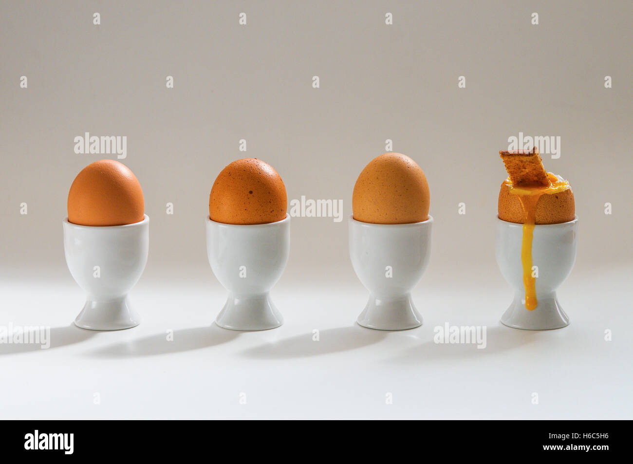 4 Eggs in egg cups, one with a toast soldier with yolk running Stock Photo