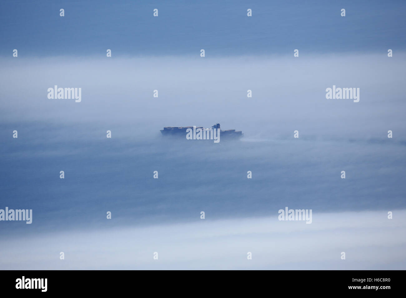 A cargo container ship sailing up the English Channel (La Manche) eastbound surrounded by low cloud and sea mist. Stock Photo