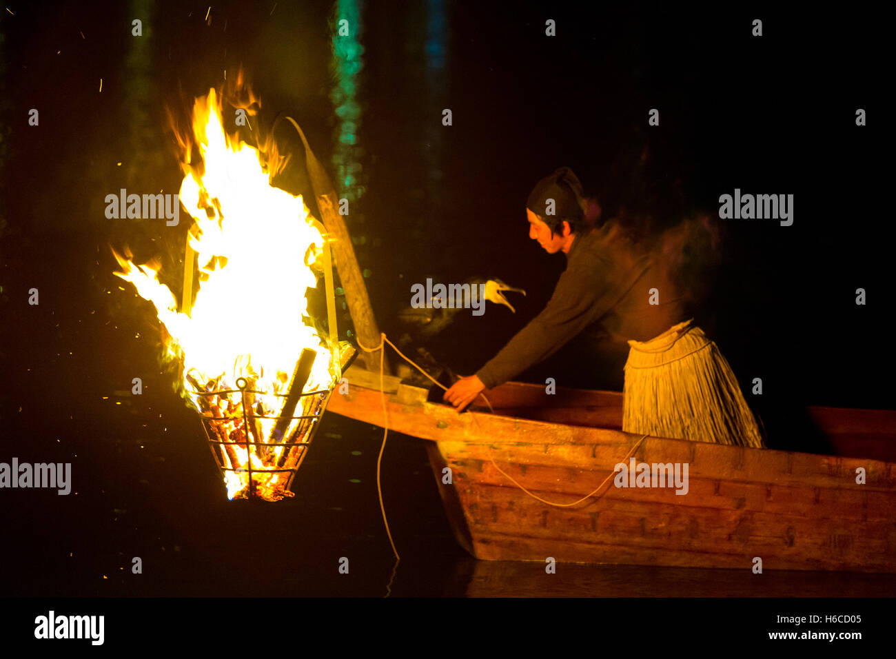 Japanese man in grass skirt, wooden boat, prepares a cormorant bird for ukai fishing drawing fish by a large flame at night Stock Photo