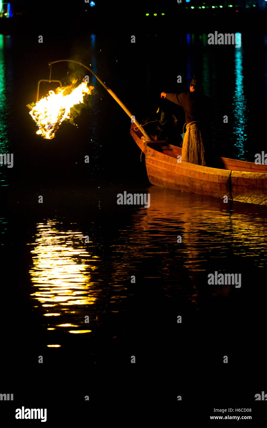 A bird on a traditional wooden boat prepares to perform ukai cormorant fishing by night flames on Kiso River in Gifu prefecture Stock Photo