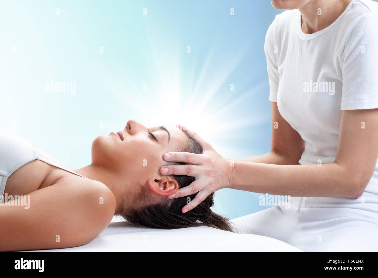 Close up portrait of therapist doing healing treatment on young woman.Therapist touching head with light glow in background. Stock Photo