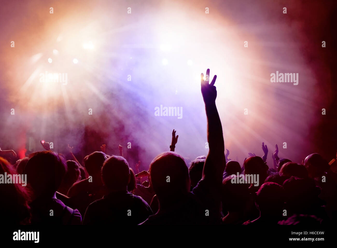 Dancing Crowd of young people dancing at disco. People Raising hands against purple and pink smoky background with light beams. Stock Photo