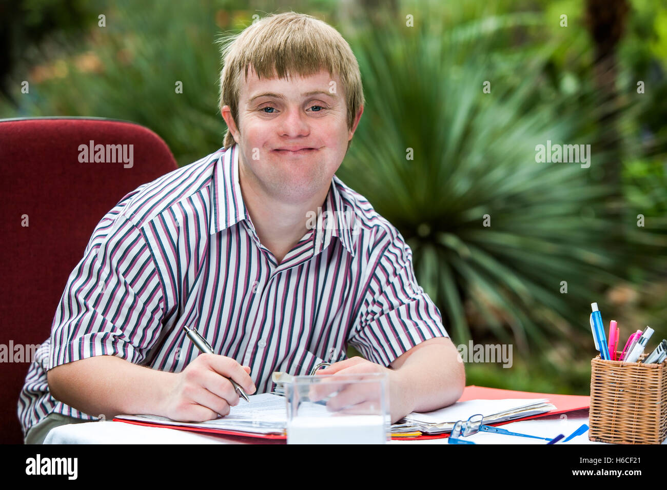 Close up portrait of young male student with down syndrome at study desk outdoors. Stock Photo