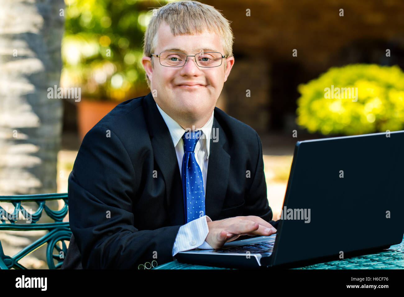 Close up portrait of young businessman with down syndrome doing accounting on laptop outdoors. Stock Photo