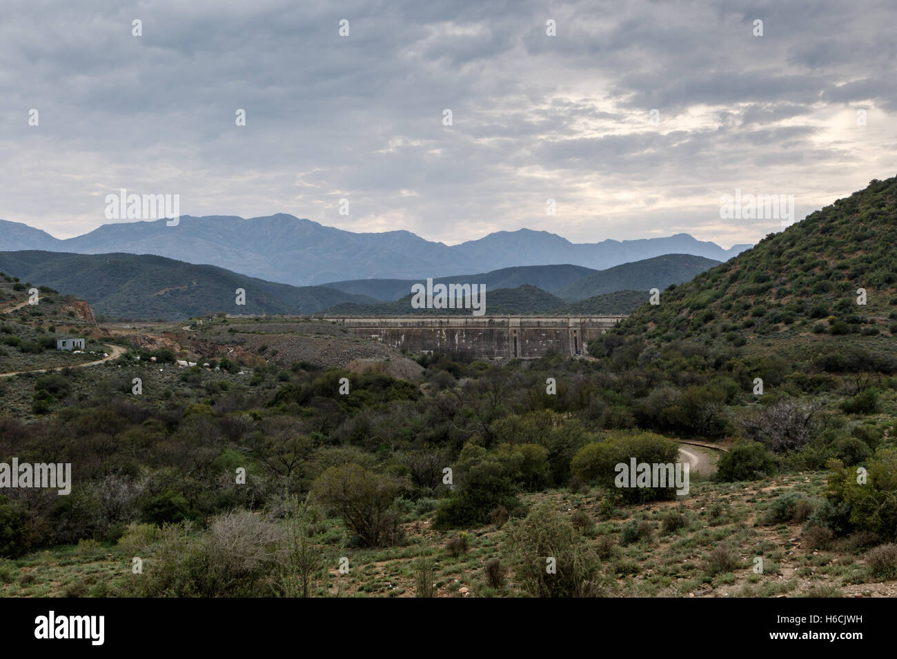 Dam wall at Calitzdorp, cloudy with mountains in the background. Stock Photo
