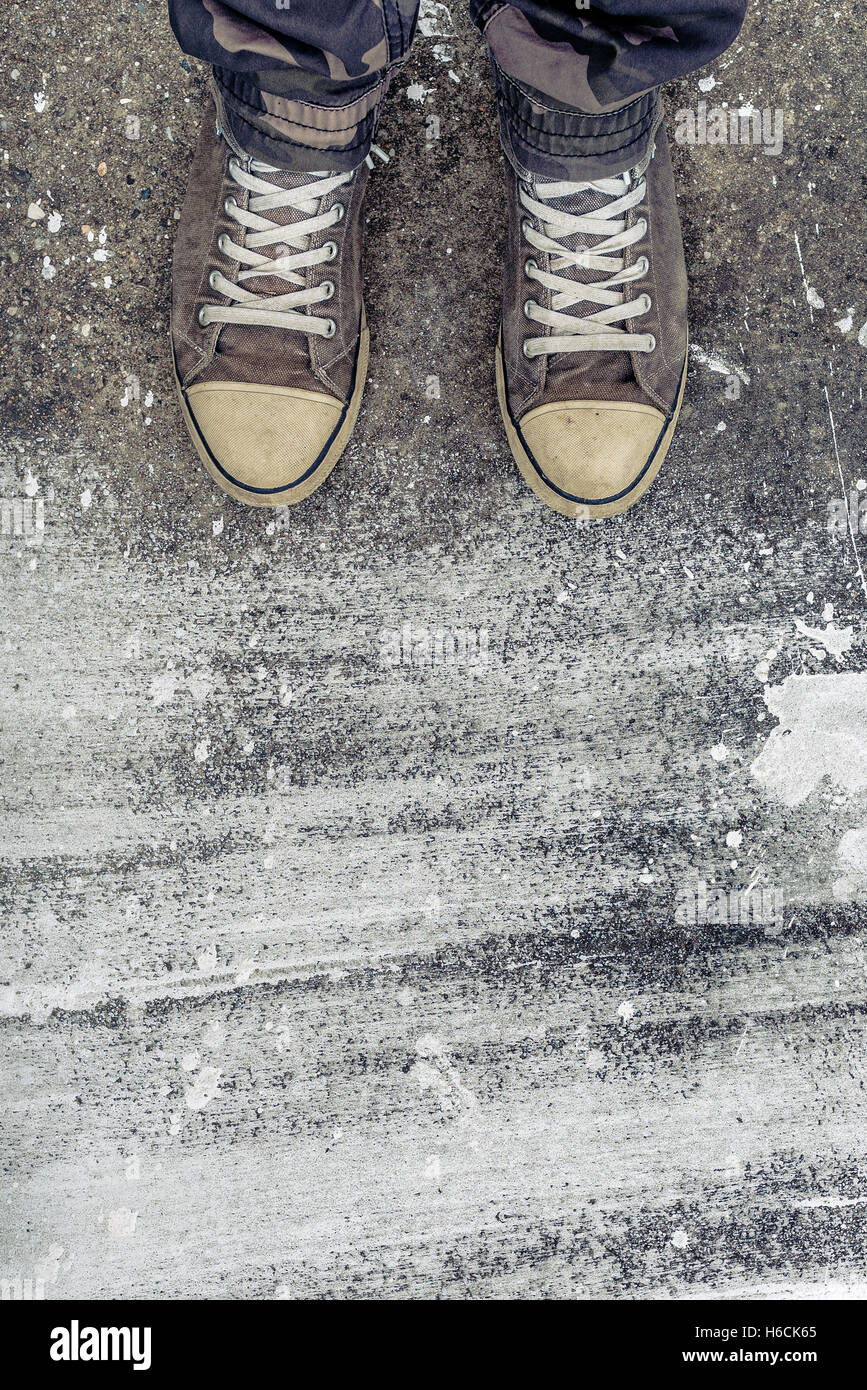 Standing on concrete floor with white drybrush stains, male feet in worn sport shoes on the street Stock Photo