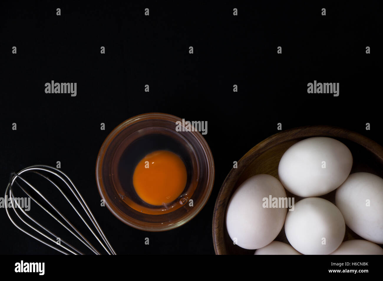 White Egg in wooden teak bowl and whisk on black background Stock Photo