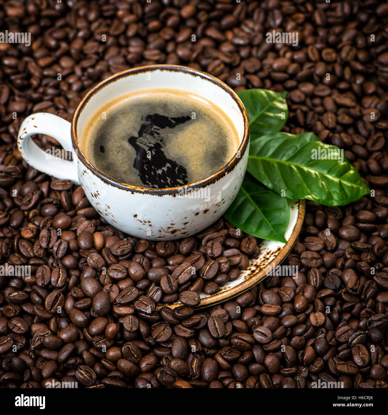 Black coffee with green leaves on caffee beans background. Vintage style toned picture Stock Photo