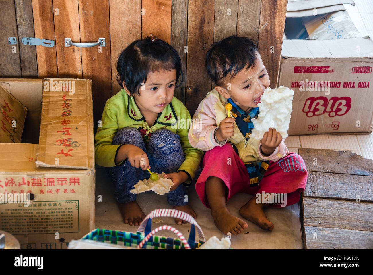 Two small children sit on the floor and eat sweets, Inle Lake, Shan