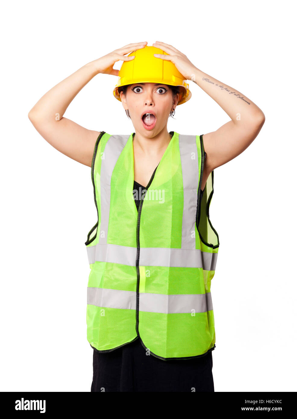 Caucasian young adult woman in her mid 20s wearing reflective yellow safety helmet and safety vest, raising her hands on her hat Stock Photo