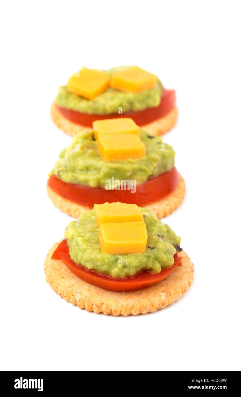 Whole grain crackers with tomato, guacamole and cheese lined up, on white Stock Photo