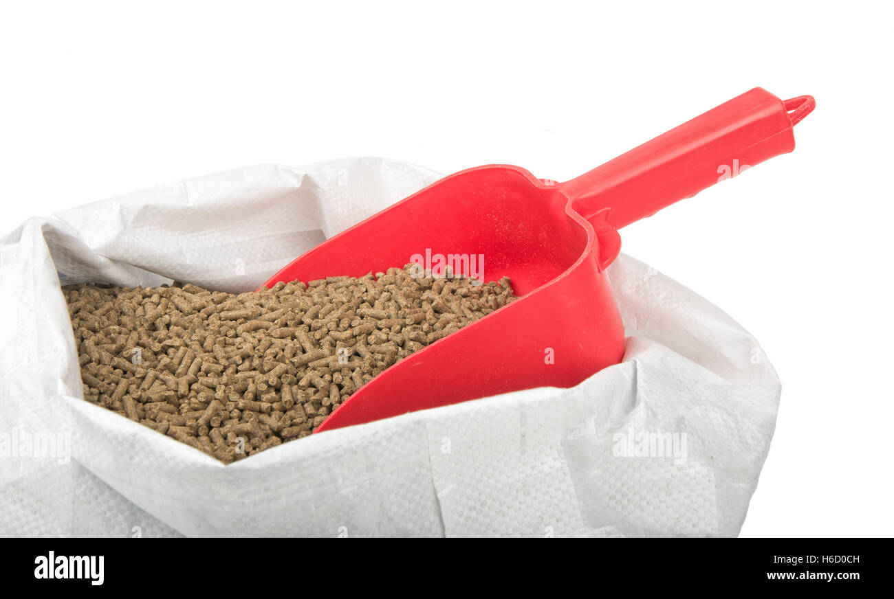 Red scoop inserted in a bagful of pelleted horse feed, isolated on white Stock Photo