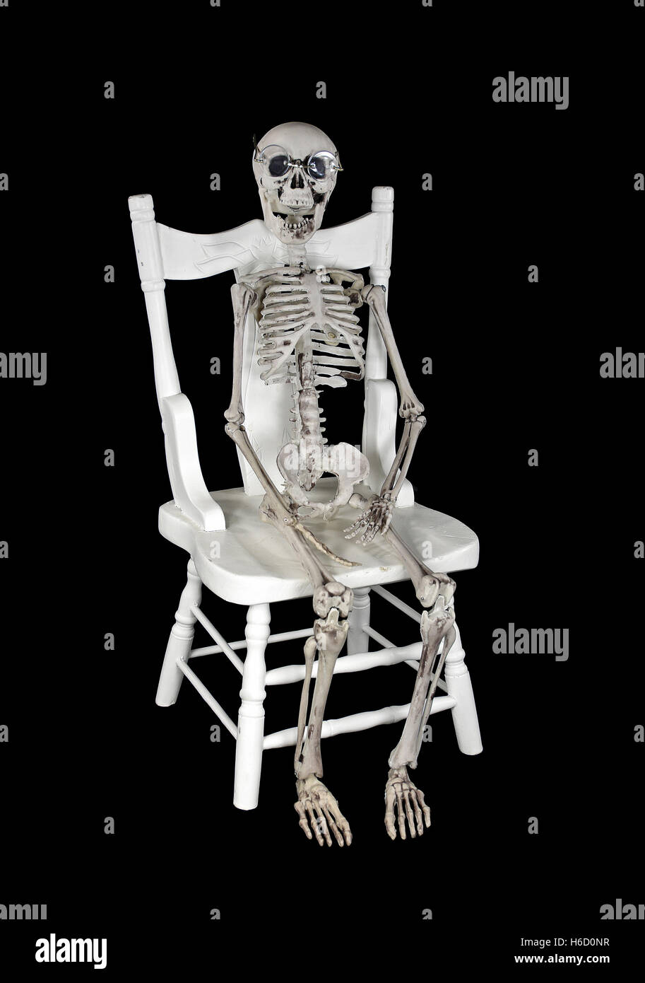 skeleton wearing glasses sitting on white wooden chair isolated on black Stock Photo