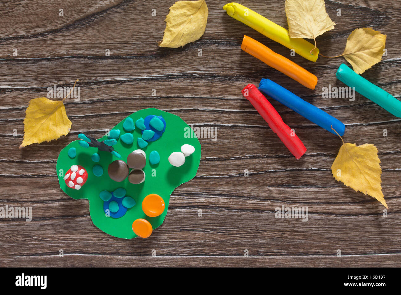 Child sculpts plasticine mushrooms tree and autumn leaves. Consumables for kids arts and crafts on a wooden table. Plasticine id Stock Photo