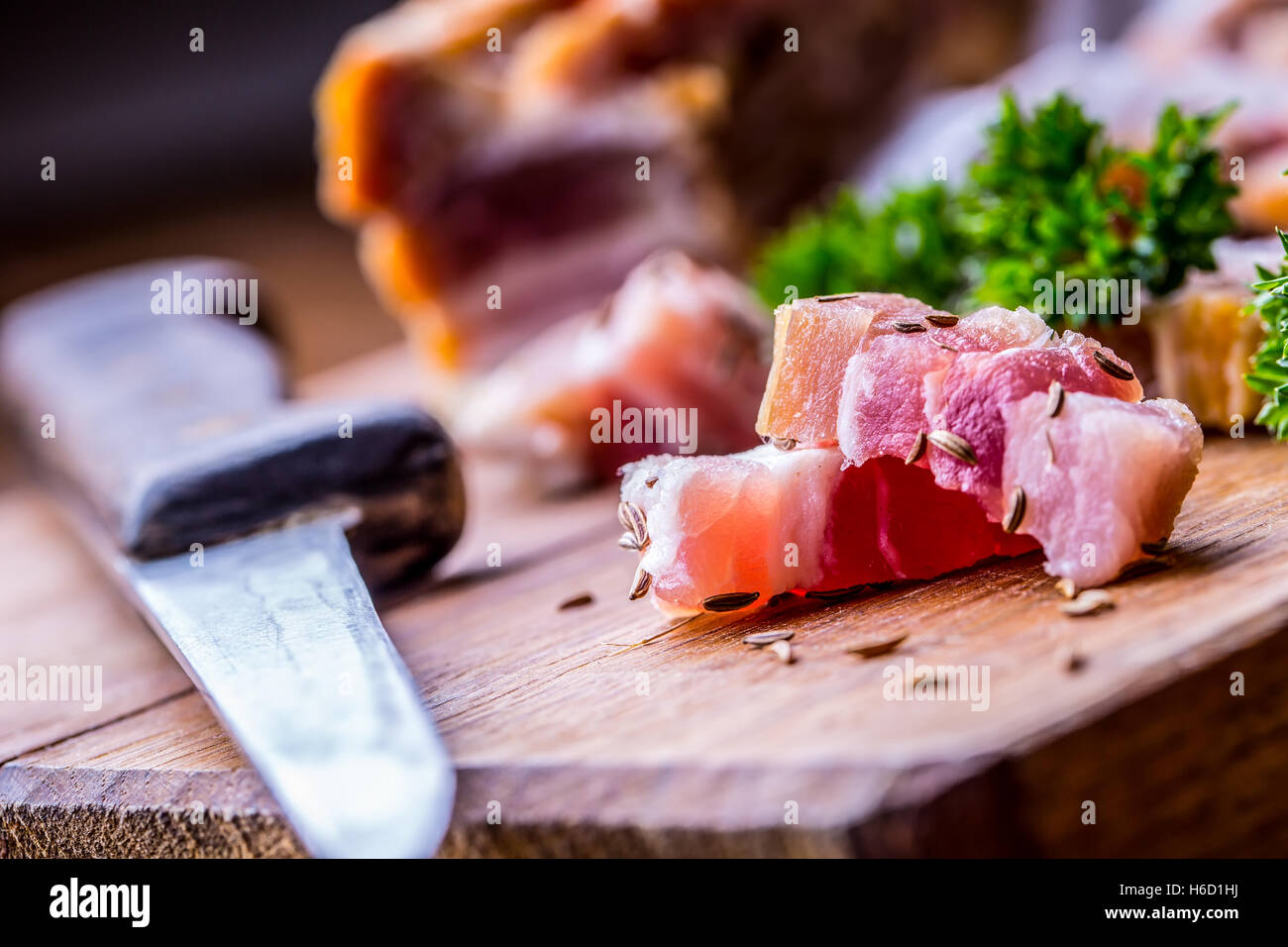 Raw smoked bacon slices on wooden board with cumin and herbs. Stock Photo