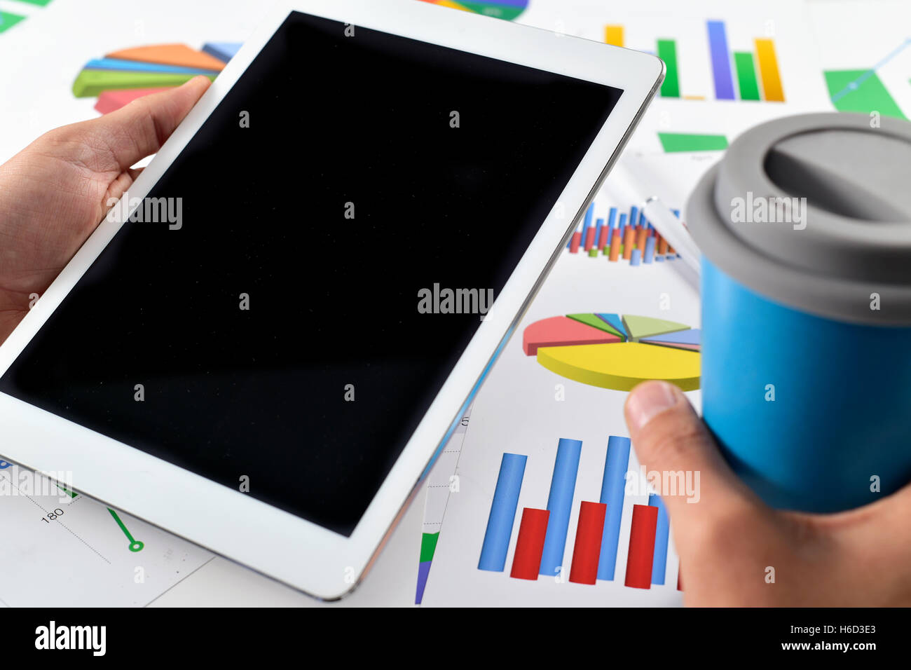 closeup of a young caucasian man at his office desk full of graphs and charts, with a cup of coffee in one hand and a tablet com Stock Photo