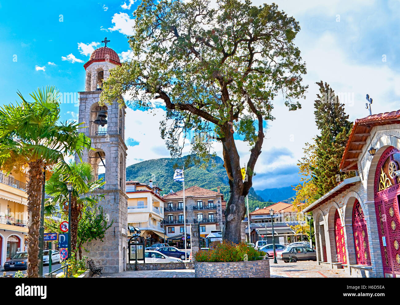 The old tree growing in the flower bed in the Agios Nikolaos church courtyard with the Mount Olympus on background, Litochoro Stock Photo