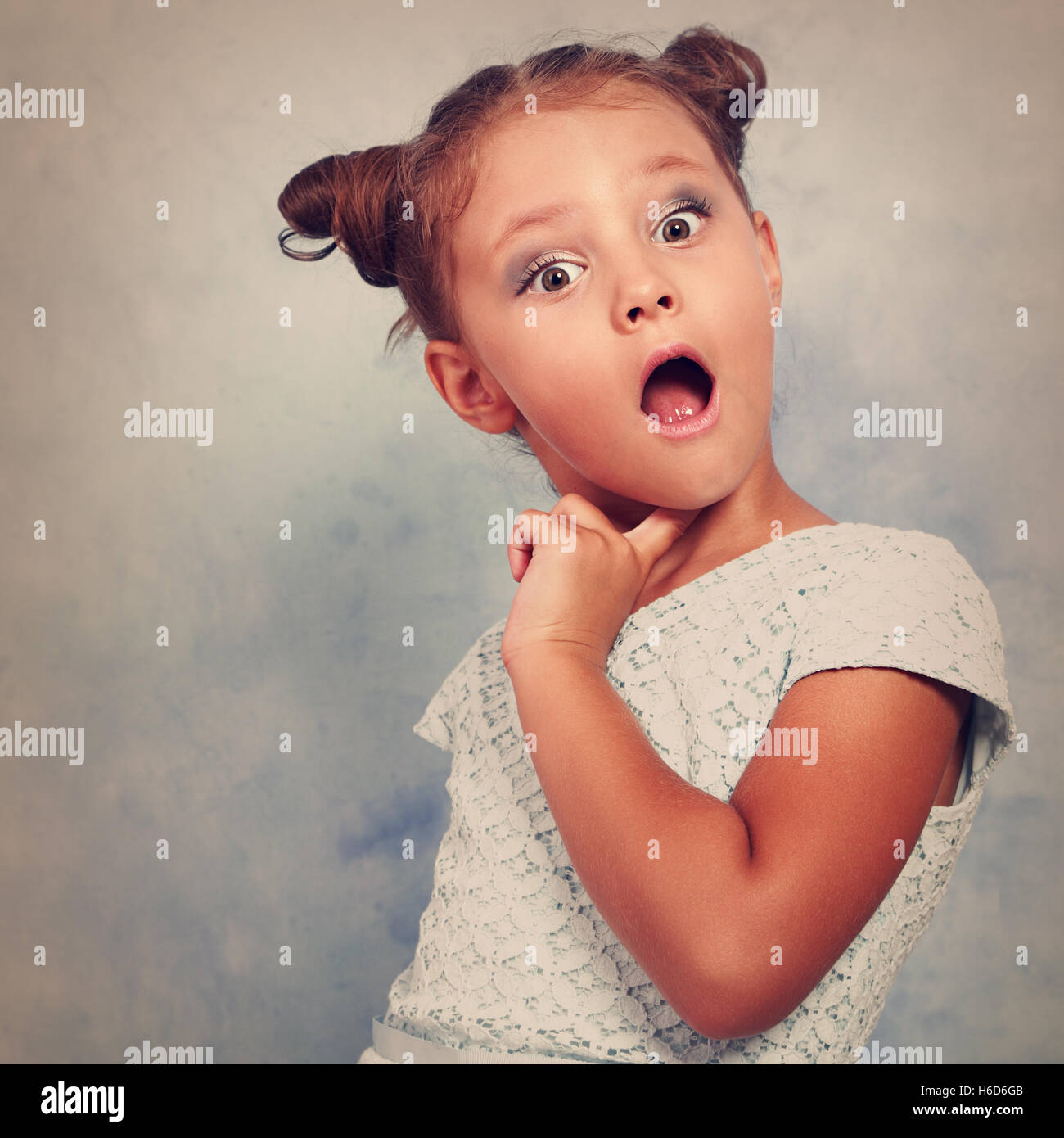 Funny surprising and very excited kid girl looking in camera on blue background. Toned closeup emotional portrait Stock Photo