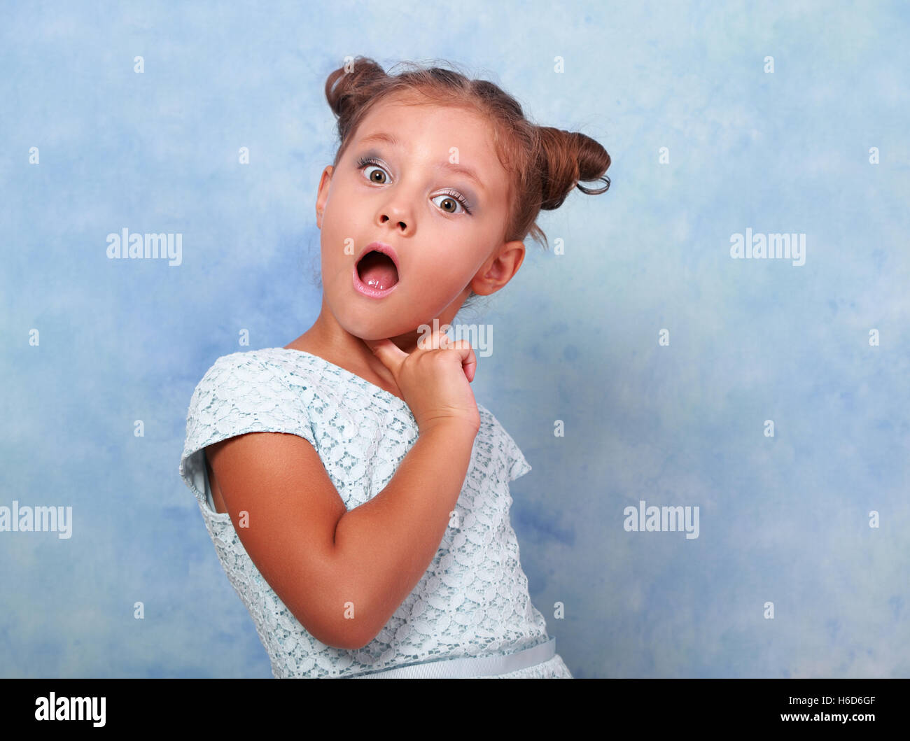 Funny surprising and very excited kid girl looking in camera on blue background Stock Photo