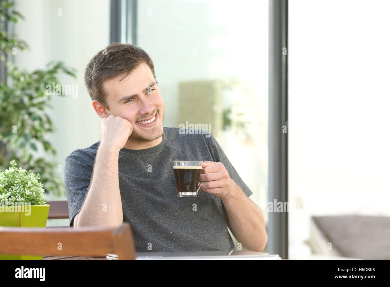 Handsome man relaxing drinking coffee sitting in a table in a balcony of an hotel room or home Stock Photo
