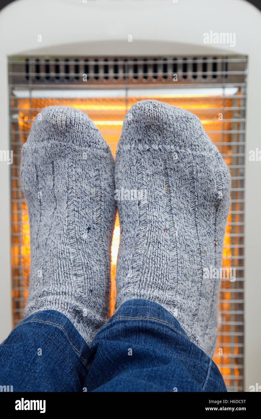 A person wearing cosy thick woolly socks warming cold feet in front of a low energy Halogen room heater to illustrate hygge. England UK Stock Photo