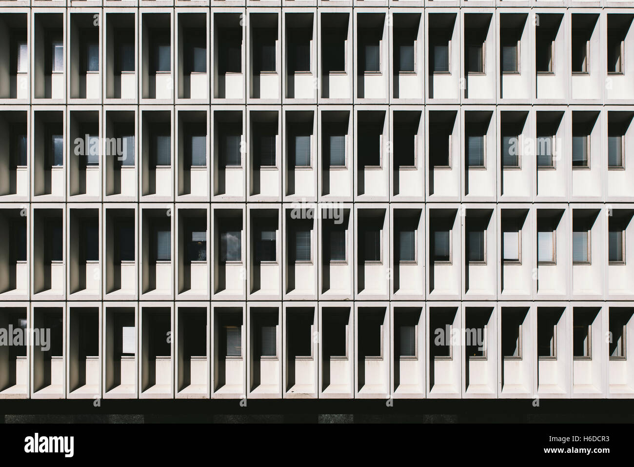 multiple small white square equal symmetrical windows on an office building with shadows. walls are white with lines pattern Stock Photo