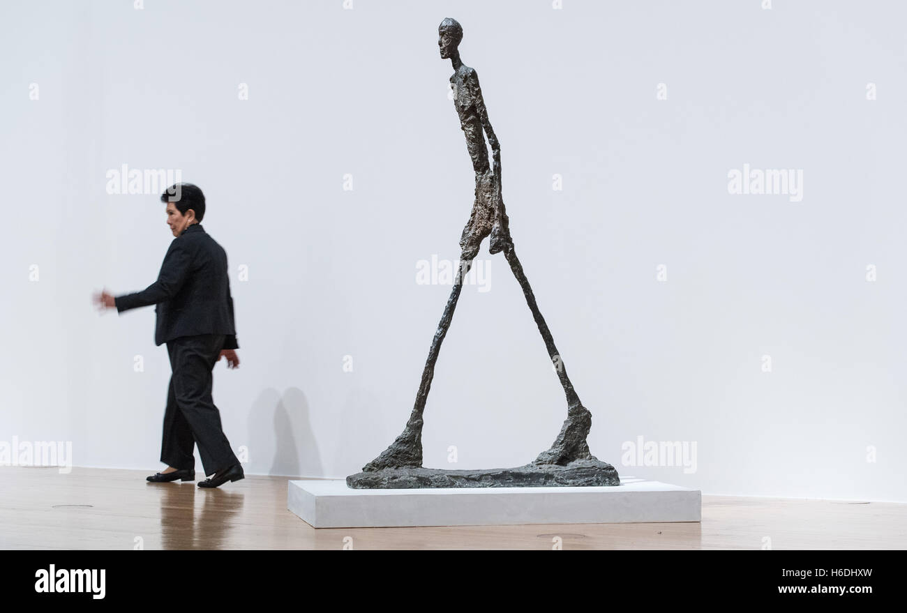 A woman walking past the sculpture 'Homme qui marche' by Alberto Giacometti at Schirn art hall in Frankfurt/Main, Germany, 27 October 2016. The Schirn art hall compares works of Alberto Giacometti and Bruce Nauman in a new double exhibition. PHOTO: BORIS ROESSLER/dpa Stock Photo