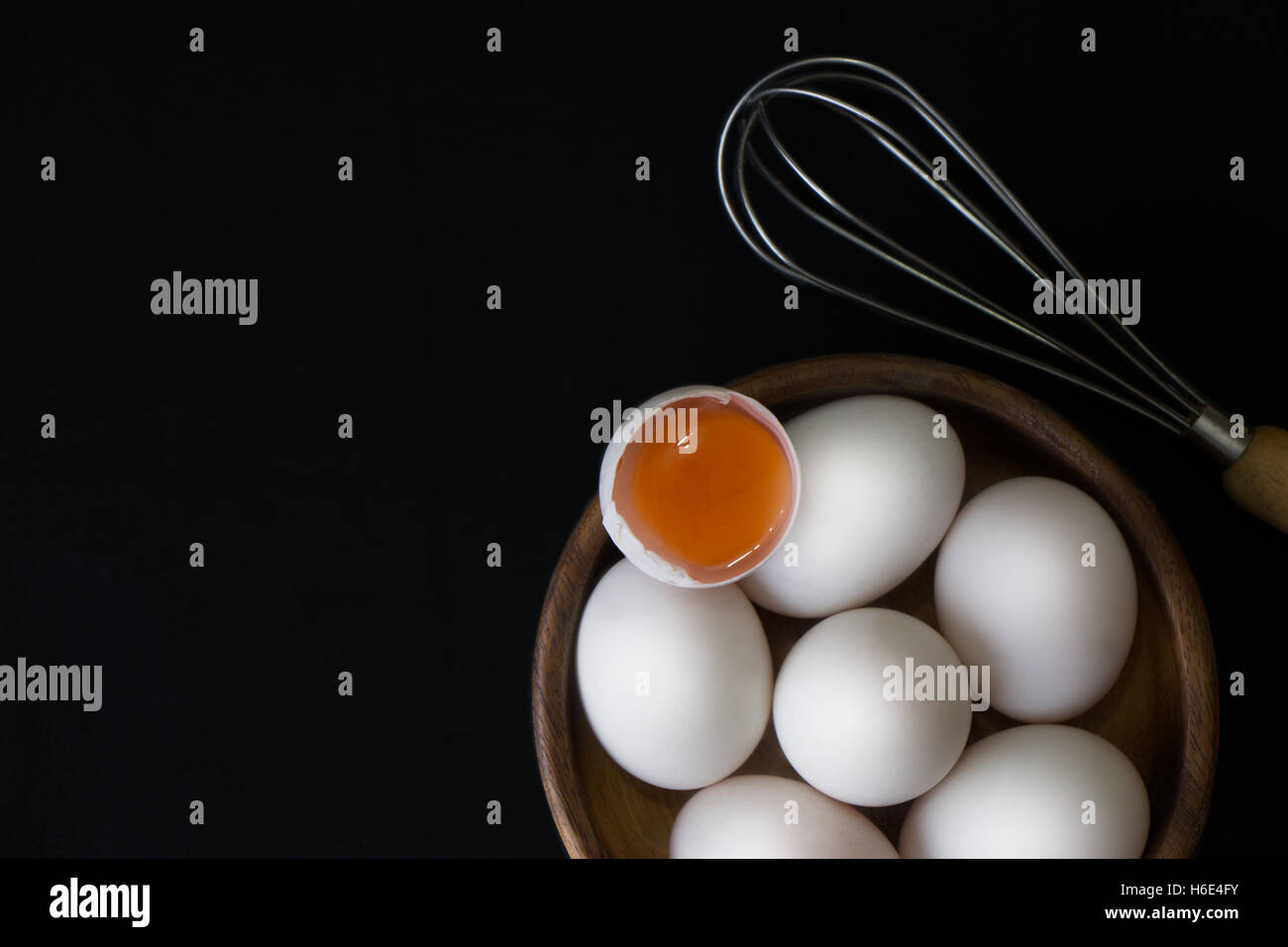 White Egg in wooden teak bowl and whisk on black background Stock Photo