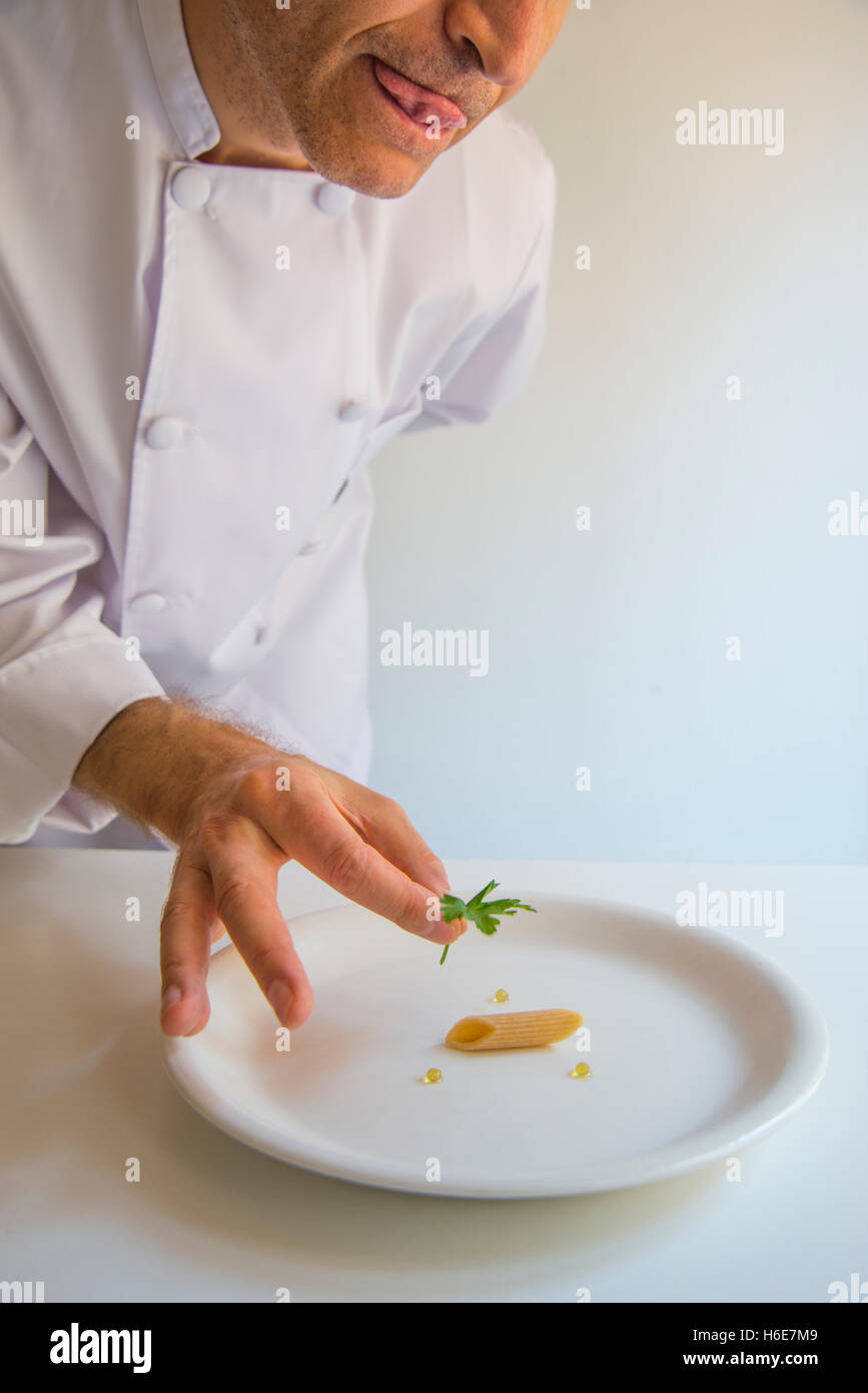 Nouvelle cuisine: minimalism. Humorous. Chef putting a leaf of parsley on top of a single macaroni. Stock Photo