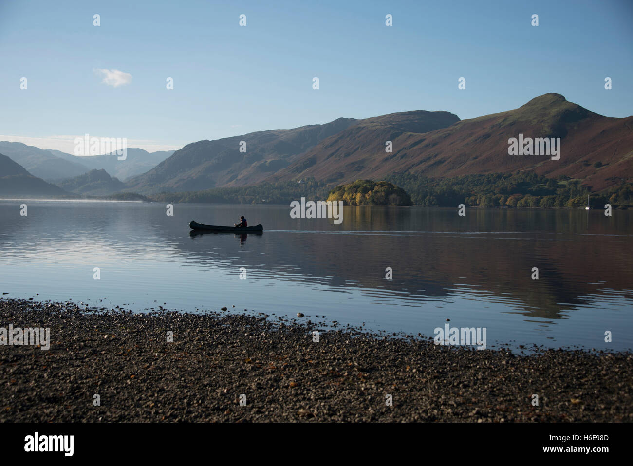 Tranquil autumnal scene at  Keswick, Derwentwater, Cumbria, UK. A lone canoeist gently paddles across the lake. Stock Photo