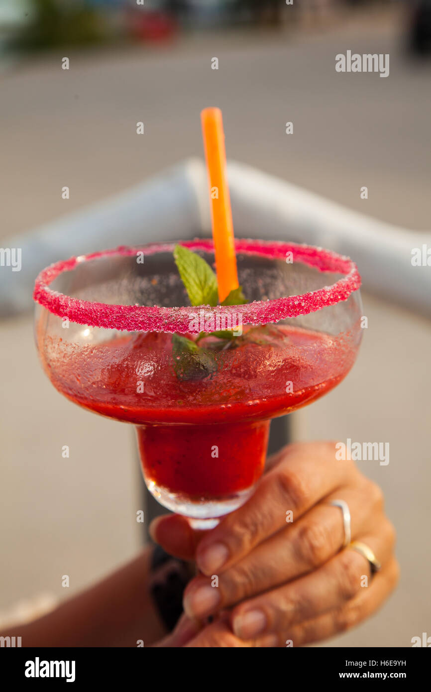 Lady holding a red alcoholic  cocktail drink with an orange straw and red sugar frosting around the rim glass Stock Photo