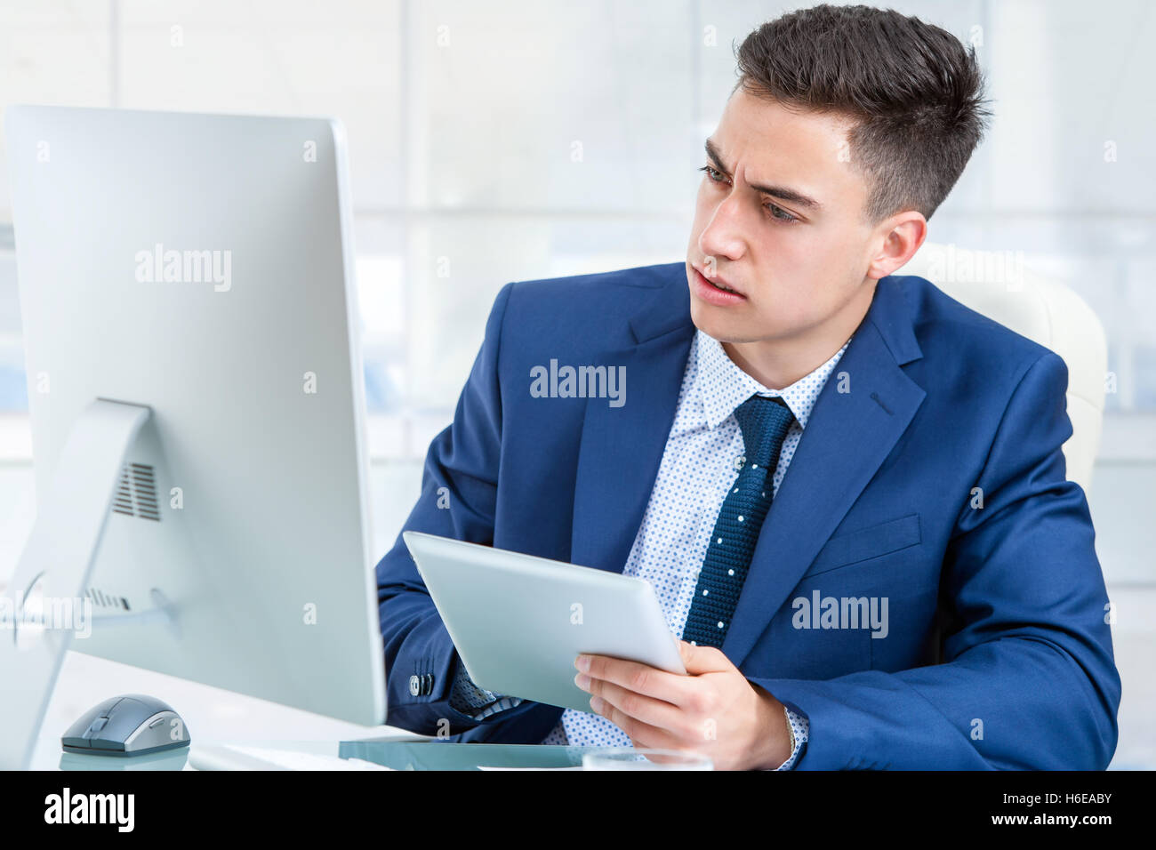 Close up portrait of young Businessman synchronizing digital tablet with computer. Young man sharing information on devices. Stock Photo
