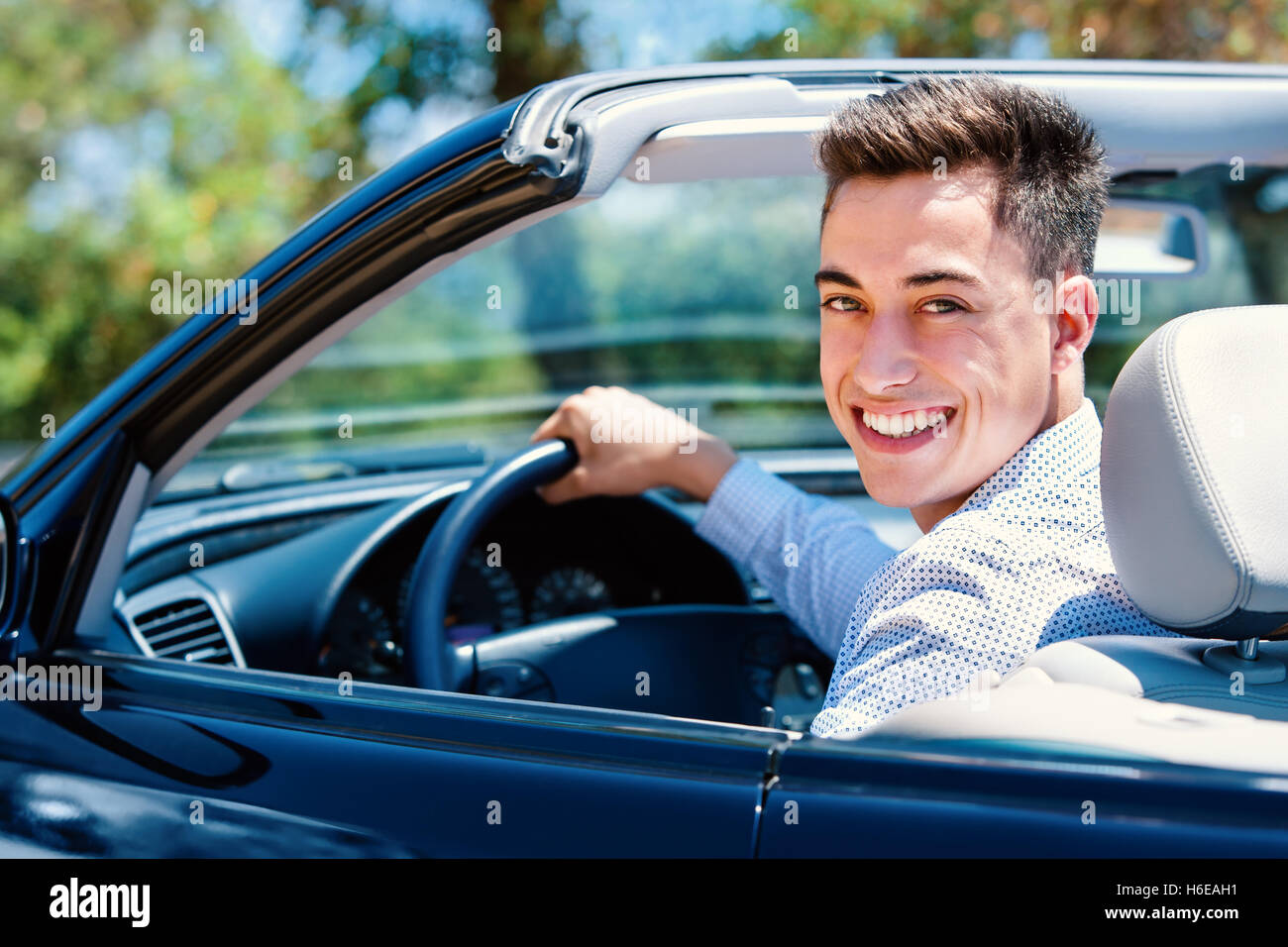 Portrait of attractive teen sitting in car. Young man sitting in convertible in driver seat. Stock Photo