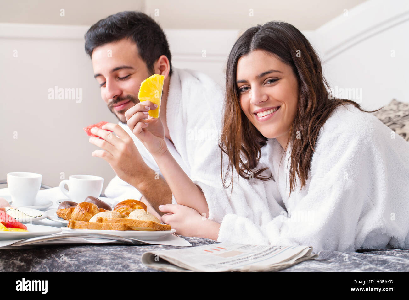 Close up portrait of couple having breakfast together on bed in hotel room.Couple wearing bathrobes. Stock Photo