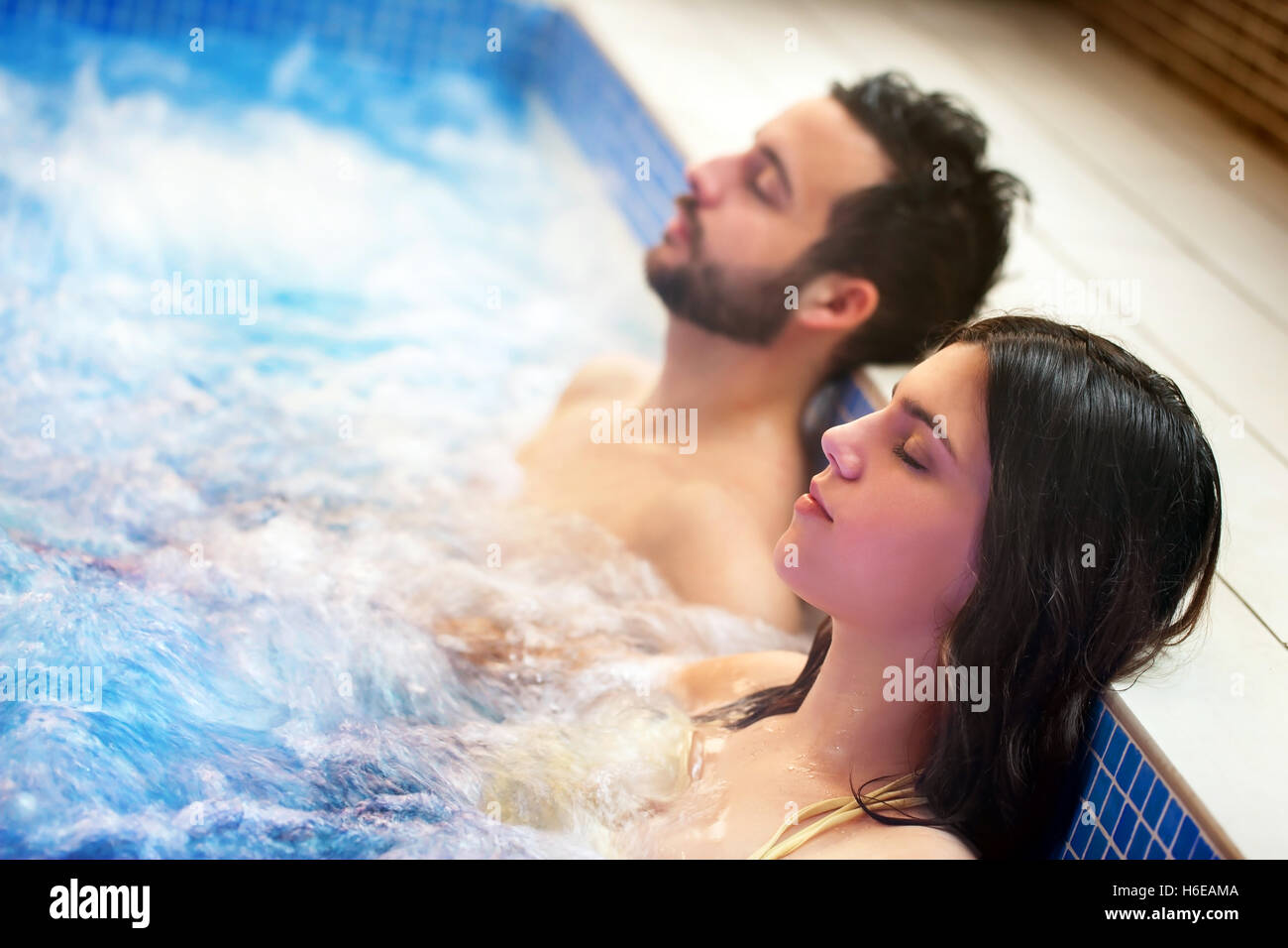 Close up portrait of young couple relaxing in spa jacuzzi. Couple together in bubble water with eyes closed. Stock Photo