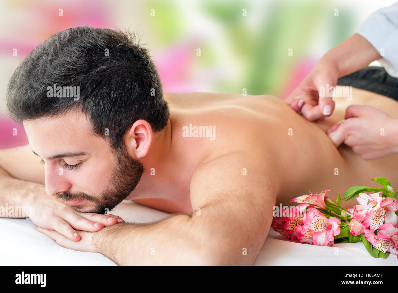 Close up of young man enjoying back massage. Young man laying face down and therapist hands massaging lower back. Stock Photo