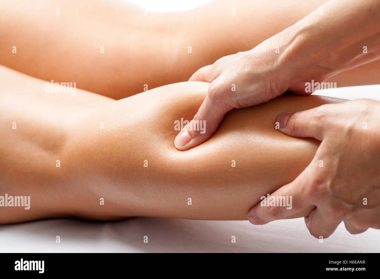 Extreme close up of osteopath applying pressure with thumb on female calf muscle. Stock Photo