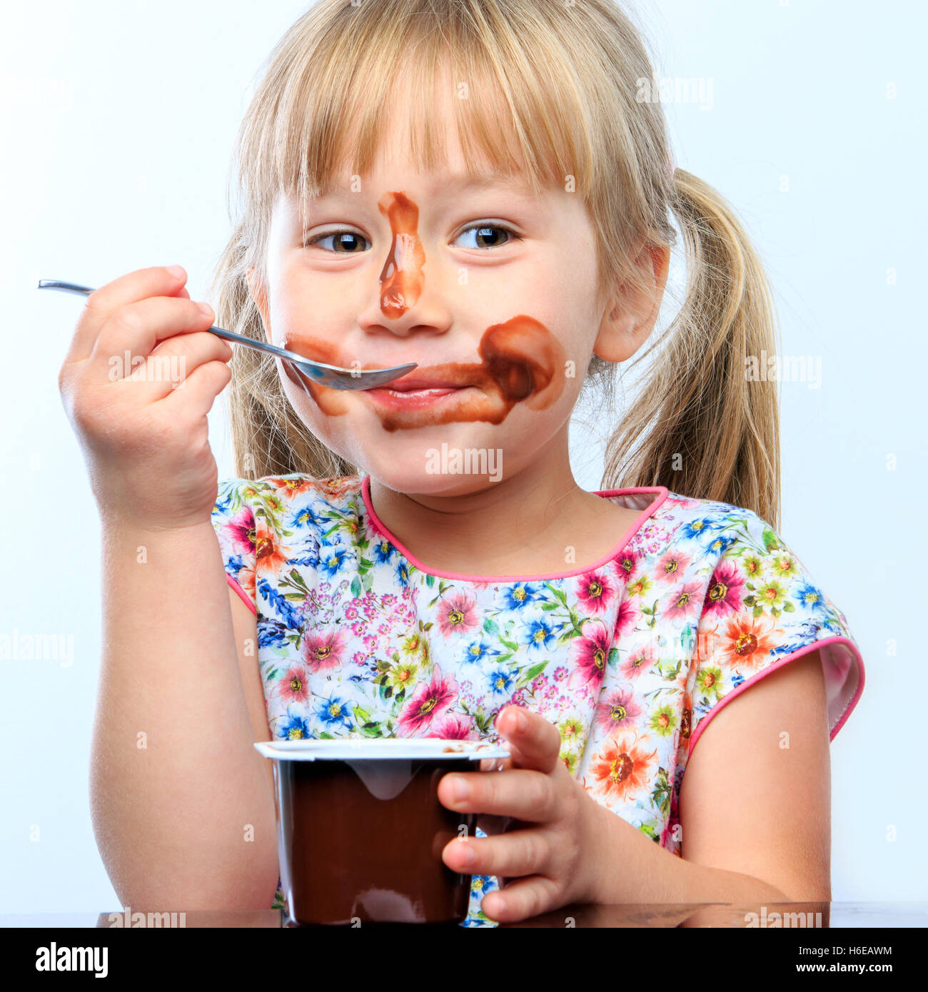 Close up portrait of Cute little girl eating chocolate yogurt at breakfast. Face messy with chocolate and funny face expresstion Stock Photo