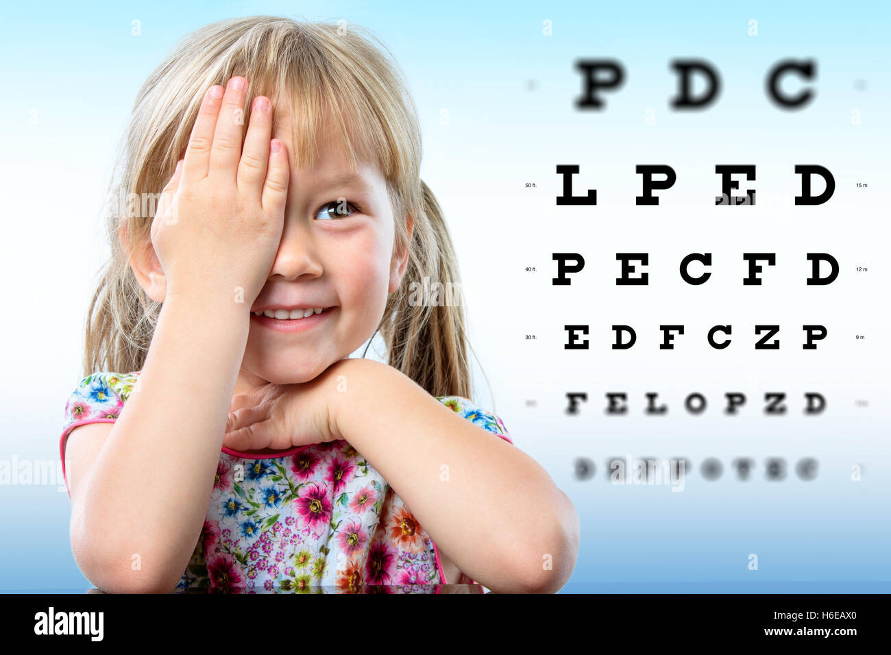 Cute little girl reviewing eyesight.Girl closing one eye with hand reading block letters on vision chart with focus point. Stock Photo