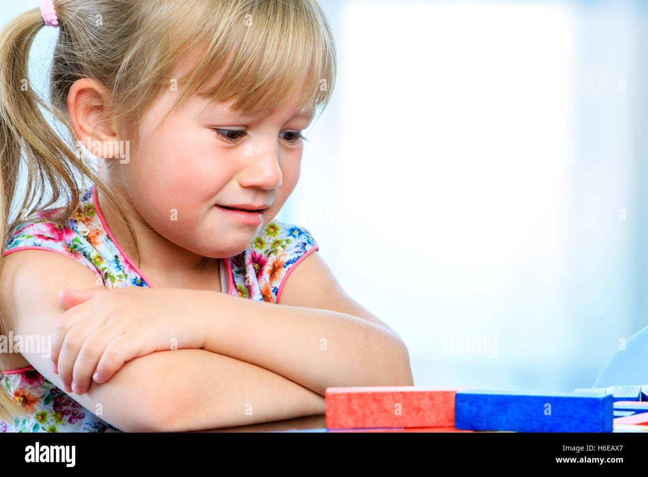 Close up portrait of unhappy little girl at table with educational game. Infant showing miserable sad face expression. Stock Photo