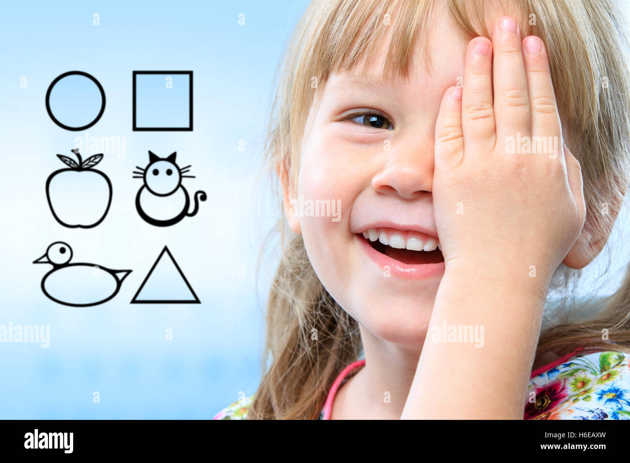 Close up face shot of little girl closing one eye with hand. Childish symbols in background as vision test chart. Stock Photo