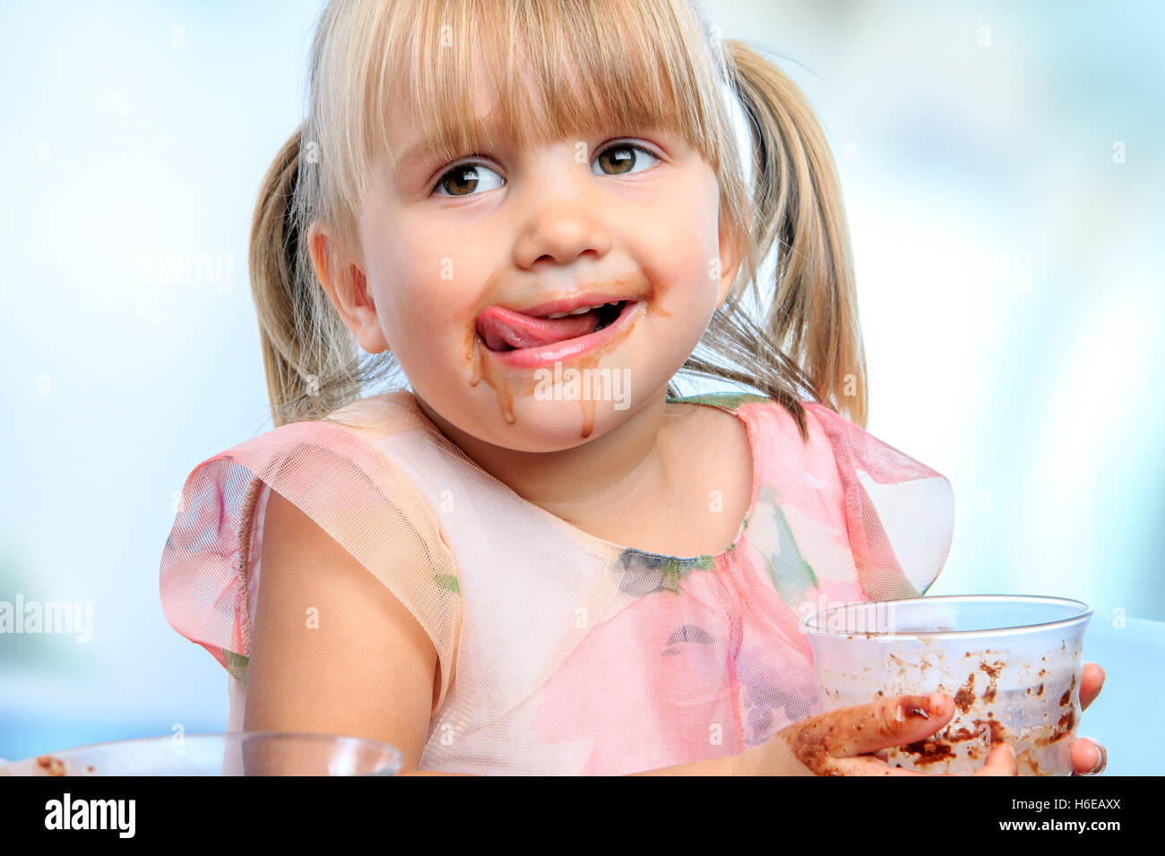 Close up portrait of Little girl with messy face drinking chocolate milkshake at home. Stock Photo