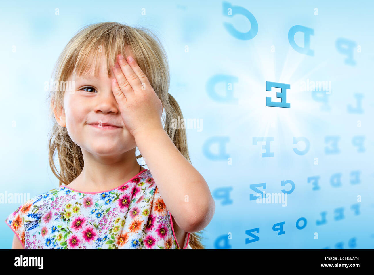Close up portrait of little girl reading eye chart. Young kid testing one eye on block letter vision chart. Stock Photo