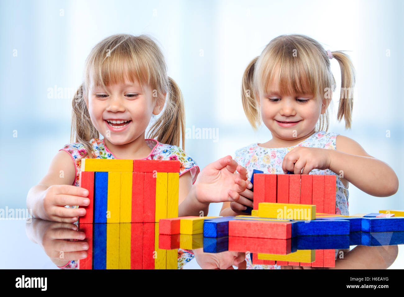 Close up portrait of two little girls playing with colorful wooden pieces at table. Stock Photo